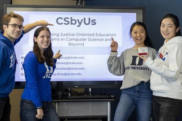 Carter Zenke with other students pointing to a screen with text that says "CSbyUS, Shaping Justice-Oriented Education Programs in Computer Science and Beyond."