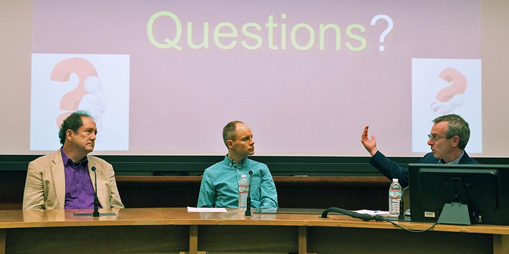 3 men in front of an audience discuss an idea