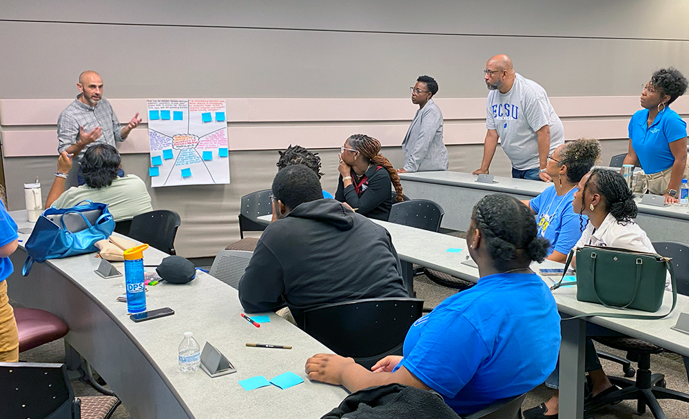 Antonio Rook looks on as Alec Greenwald addresses student researchers during a team meeting.