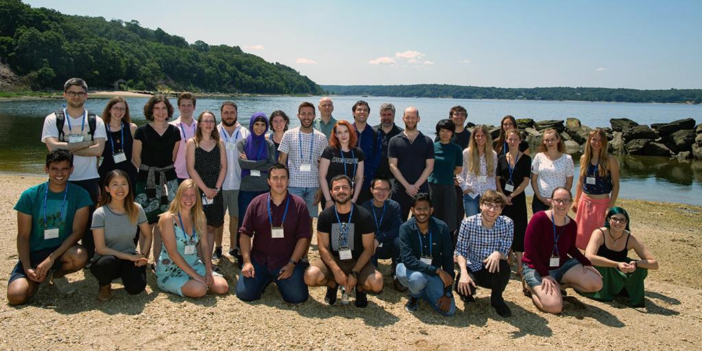 A group of people stand and smile near a lake