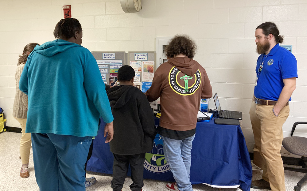 Adults and children visit a resource table to learn more about the local library.