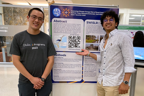 Two students smile and pose in front of their poster.