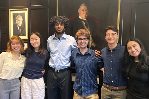 Student team members pose with their arms around each other in front of a painting.